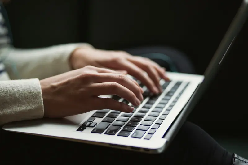 A person typing on a laptop, representing a student drafting a college essay